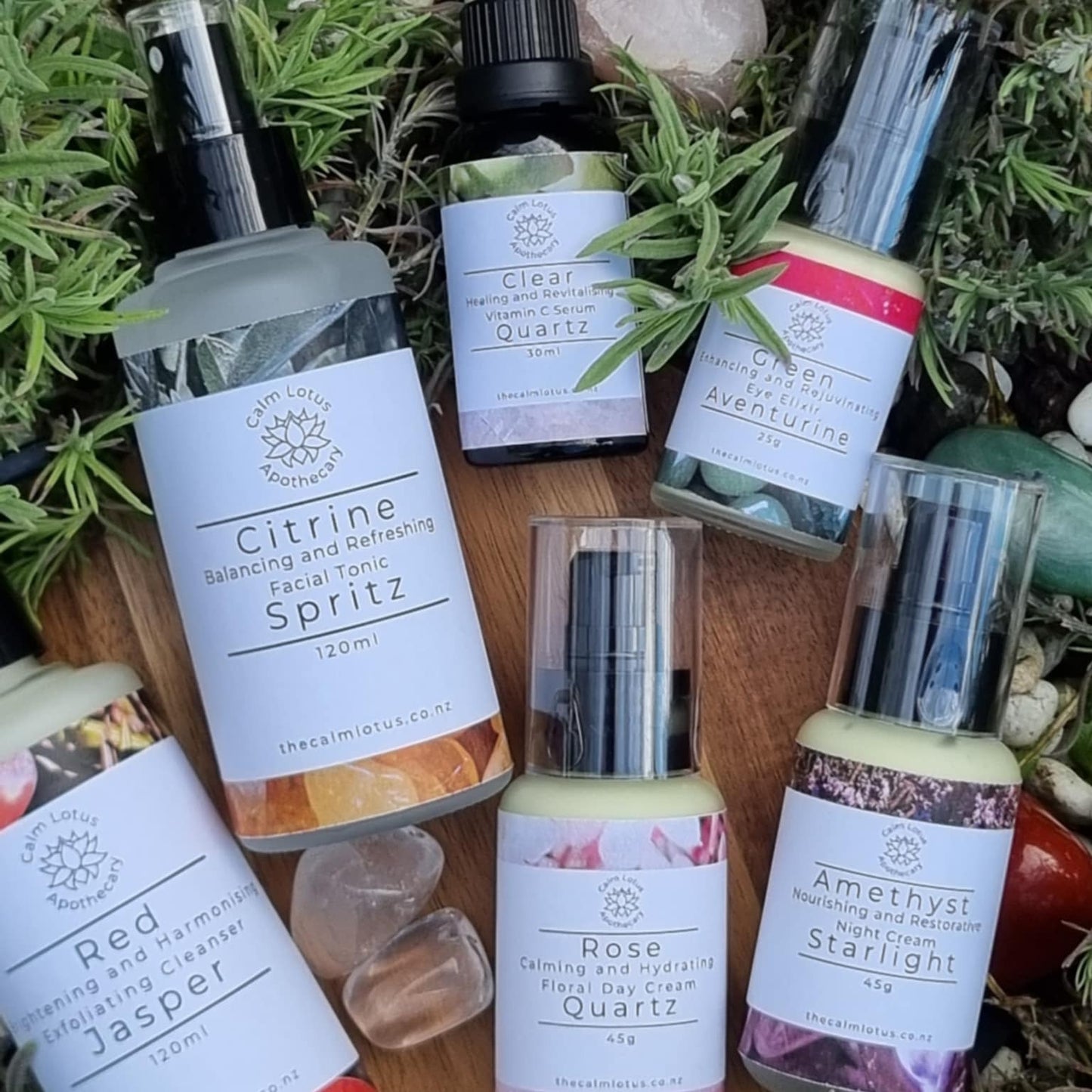 Collection of natural skincare products with labels on a wooden surface surrounded by greenery.