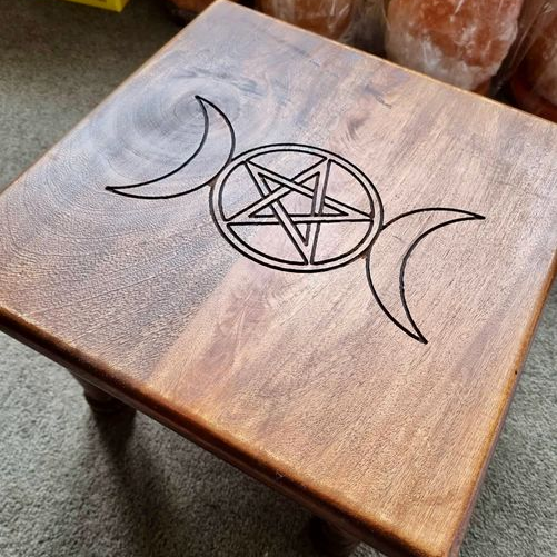 Wooden table with a pentagram and moon symbol design on a carpeted floor.