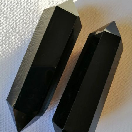 Two black, faceted crystal wands on a textured white surface