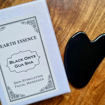 Black Onyx Gua Sha tool next to its packaging on a wooden surface