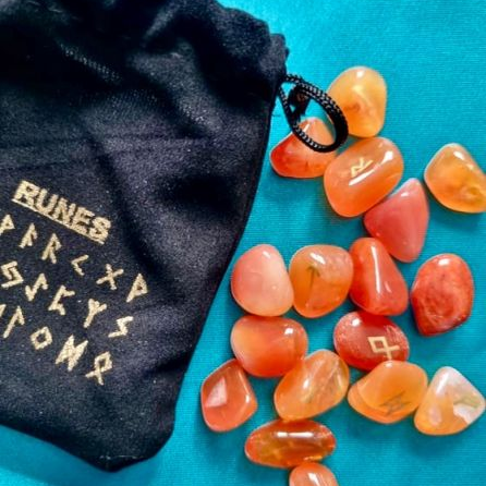 Orange stones with runic symbols next to a black drawstring bag on a blue background