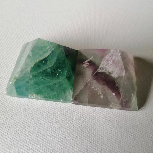 Two crystal pyramids, one green and one multicolored, on a white background