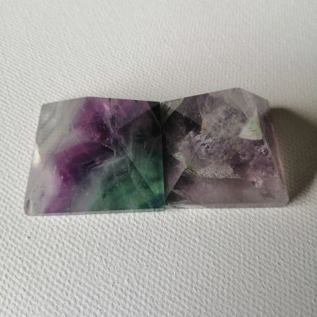 Two polished gemstone pyramids with purple and green hues on a white background
