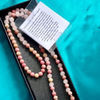 Colorful mala bead necklace with a pendant in a black box on a teal background