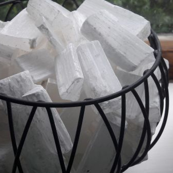 Selenite blocks in a black wire basket lamp on a light surface.