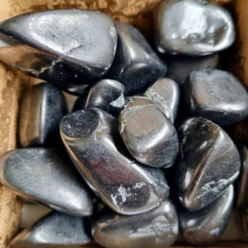 Box filled with dark gray tumble stones on a cardboard background
