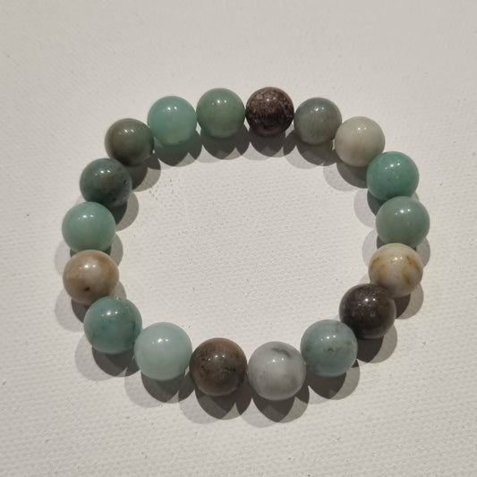 A beaded stretch bracelet made of polished round amazonite gemstone beads in shades of mint green, gray, brown, and beige, arranged in a circle on a light off-white textured background.