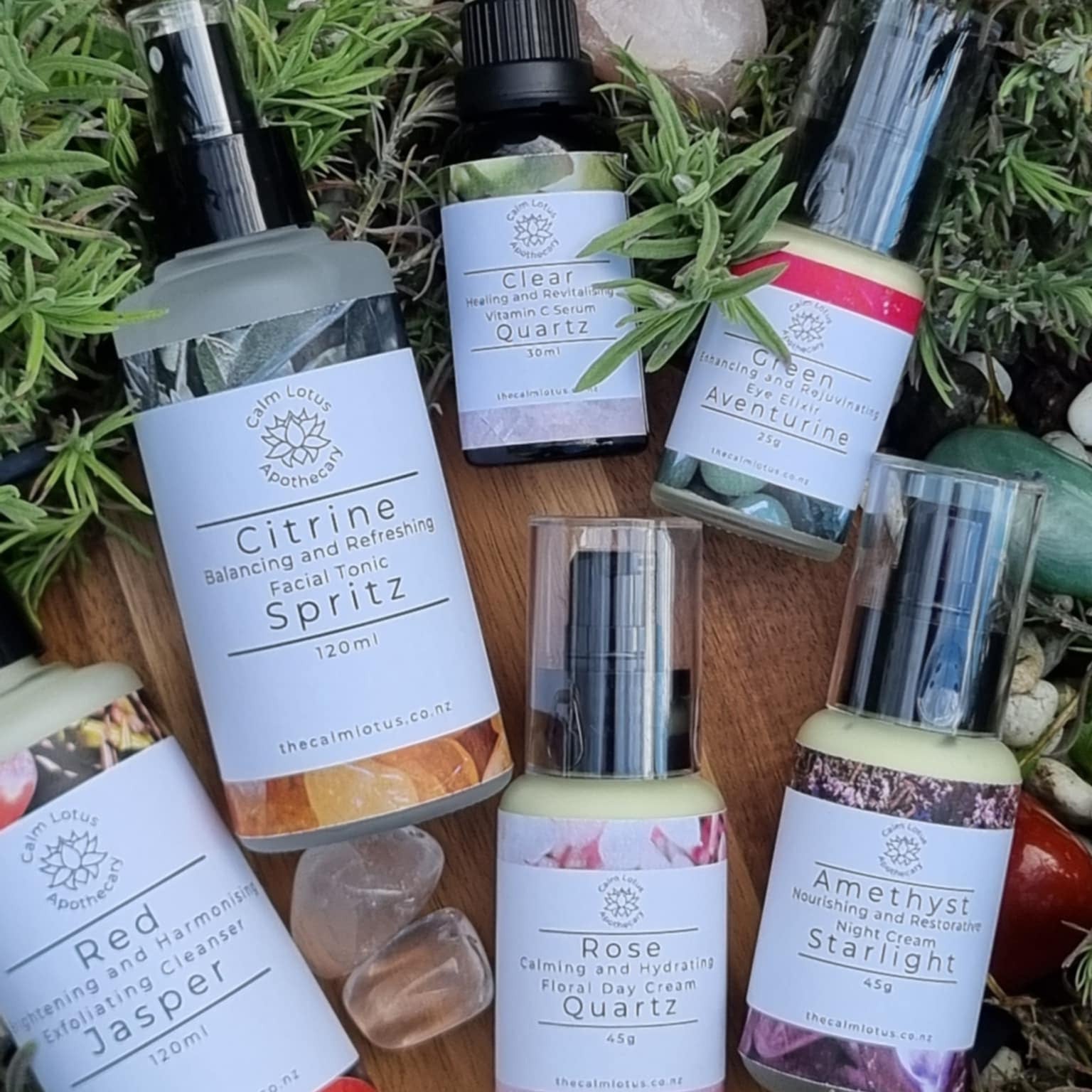 Collection of natural skincare products with labels on a wooden surface surrounded by greenery.