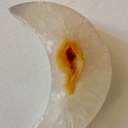 Semicircular moon shaped piece of quartz  with a central brownish-orange spot on a light background