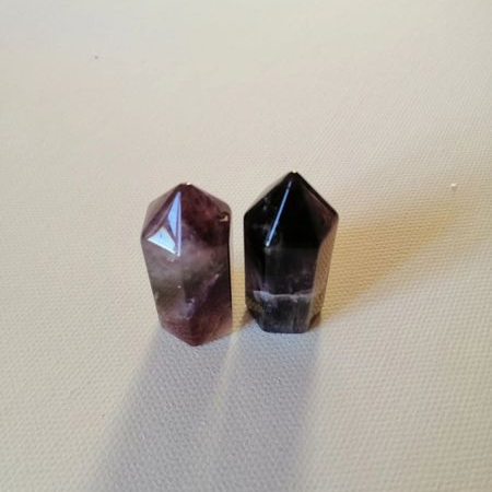 Two faceted purple crystal points on a beige fabric background