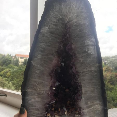 Amethyst crystal geode held by a hand with a blurred outdoor background