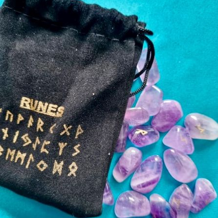 Black drawstring bag with gold rune text and purple crystal stones on a teal background