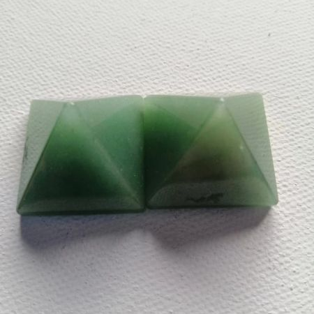 Two green pyramid-shaped stones on a textured white surface
