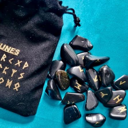 Black stones with runic inscriptions next to a black drawstring bag on a blue background
