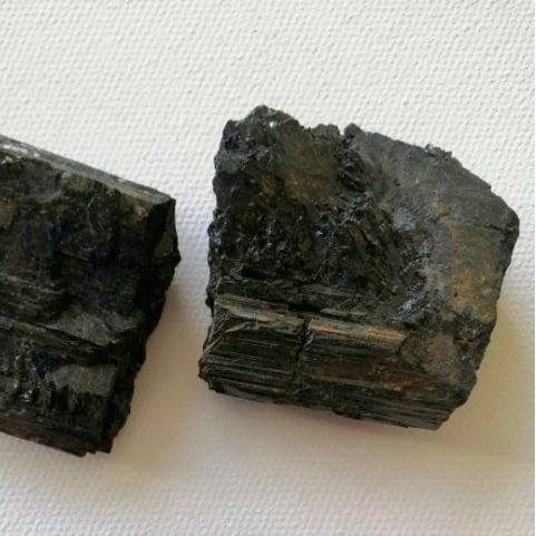 Two dark raw pieces of tourmaline on a white background.