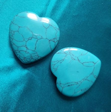 Two turquoise heart-shaped stones on a blue fabric background