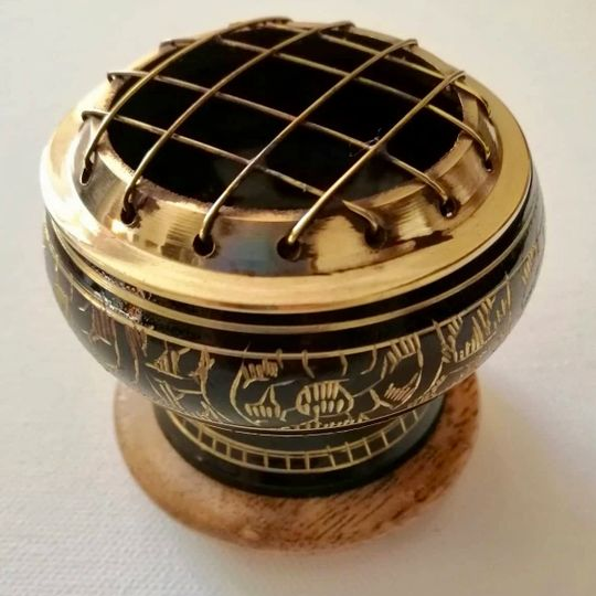 Decorative metal incense holder with intricate designs on a white background