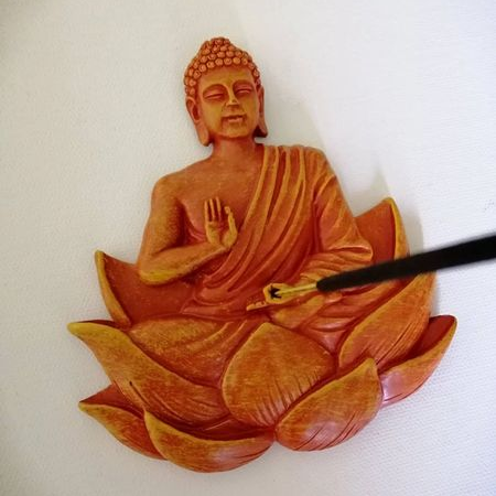 Flat orange mold of a Buddha seated in a lotus flower with an incense stick in the centre.