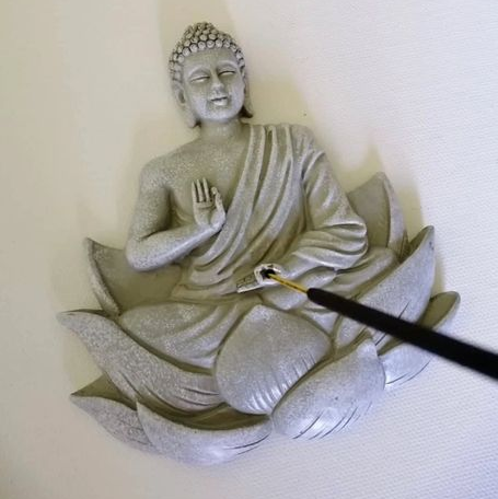 Flat grey mold of a Buddha seated in a lotus flower with an incense stick in the centre.