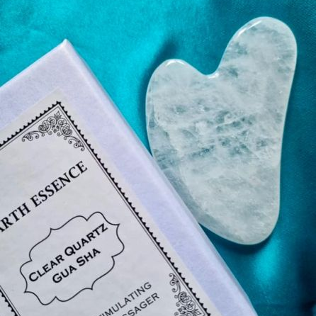 Clear quartz Gua Sha tool on its packaging with a blue background