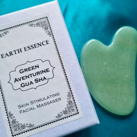 Green Aventurine Gua Sha tool next to its packaging on a blue background