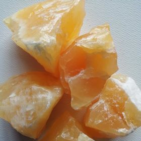 Close-up of raw orange calcite pieces on a white background