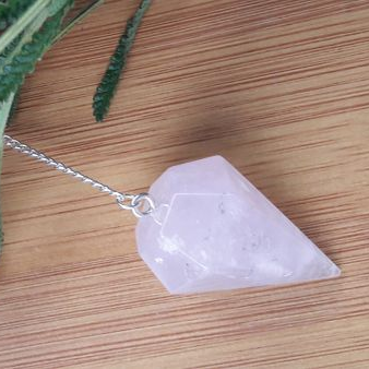Crystal pendulum on a chain on a wooden surface with greenery