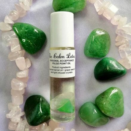 Roll on bottle of Personal Acceptance pulse point oil with green stones and a necklace on a light background