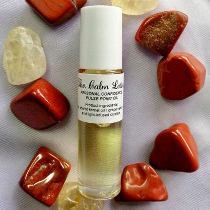 Roll-on bottle of Personal Confidence pulse point oil surrounded by red and yellow stones on a white fabric background