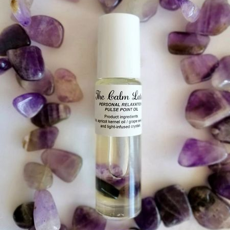 Roll-on bottle of Personal Relaxation pulse point oil surrounded by purple crystals on a white background