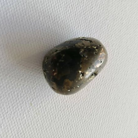 Pyrite tumblestone stone on a textured white surface