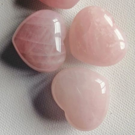 Four pink heart-shaped stones on a textured white surface