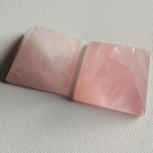 Two pink pyramid shaped crystals on a textured white surface
