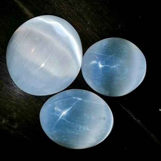 Three Selenite palmstons on a dark surface