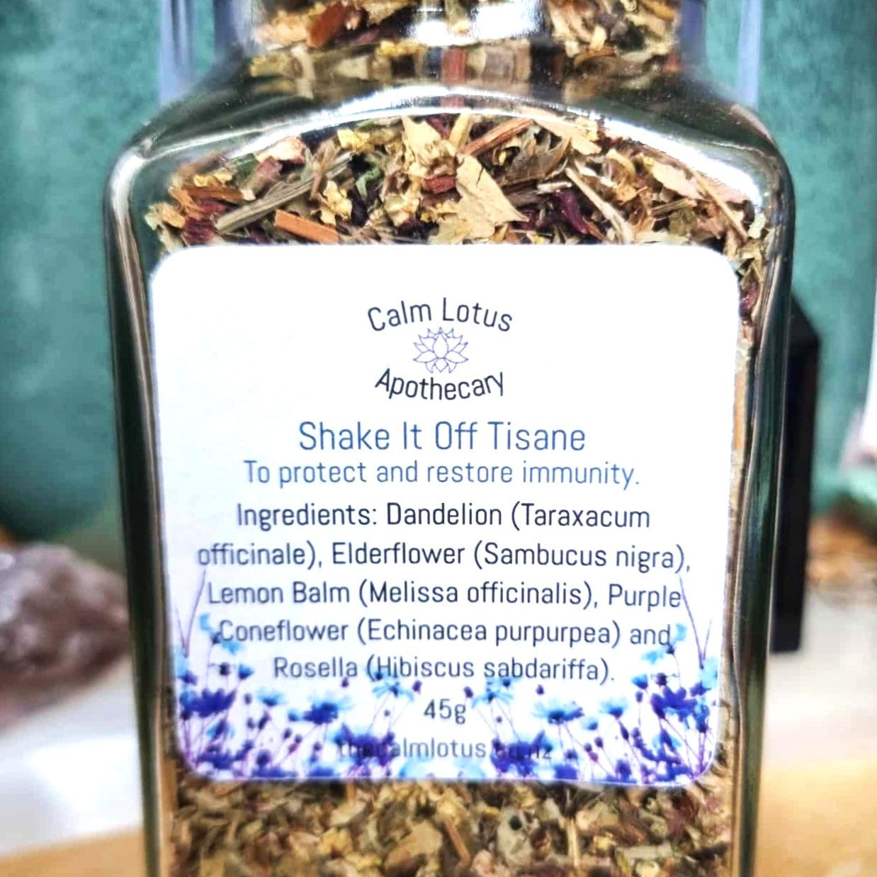 Jar of Calm Lotus Apothecary 'Shake It Off Tisane' with a label on a wooden surface.