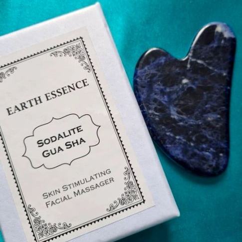Sodalite Gua Sha skin stimulating facial massager with packaging on a teal background