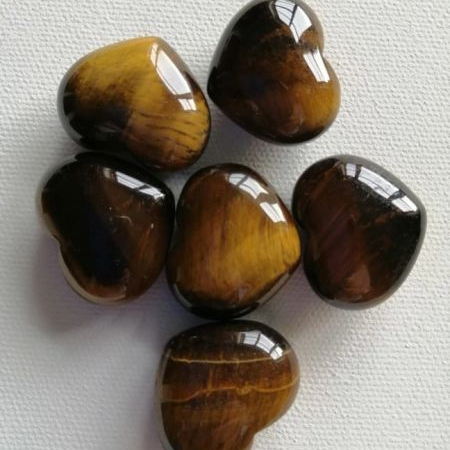 Six tiger's eye heart shaped stones arranged on a white fabric background