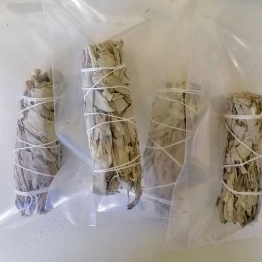 Four bundles of sage wrapped in twine on a white background